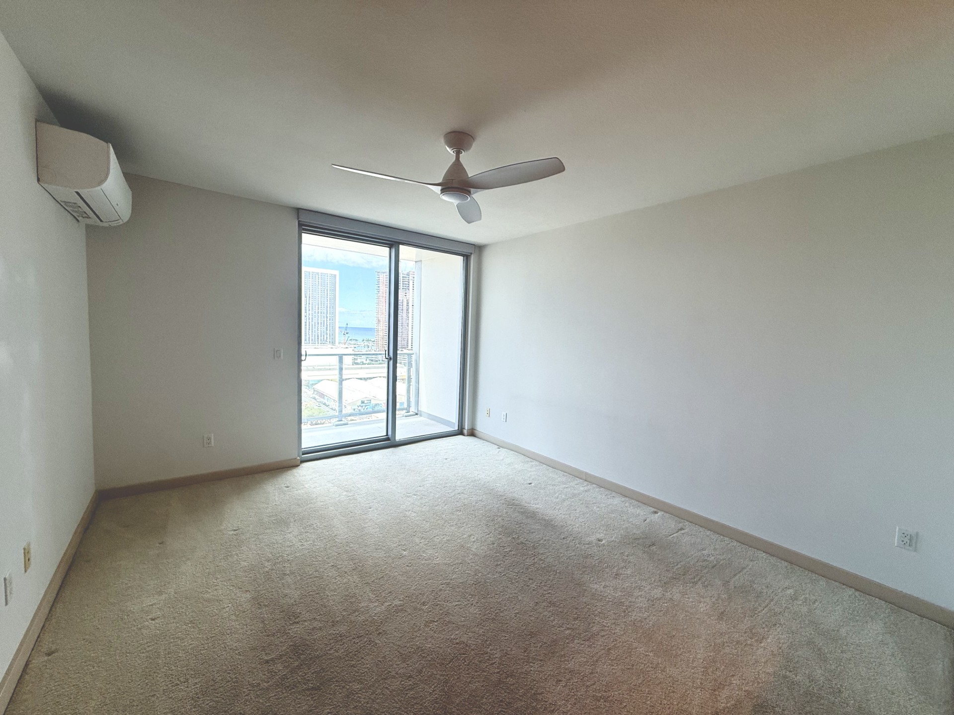 A room with a ceiling fan and a window with a view of a city.